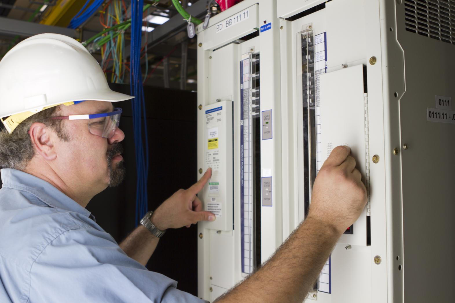 A male electrician inspects and electrical control panel.