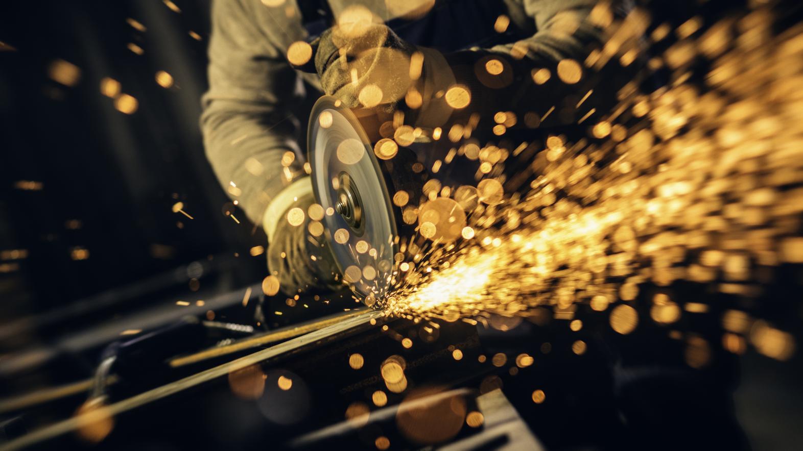 A man uses an angle grinder to cut steel on the jobsite, causing sparks to fly toward the camera