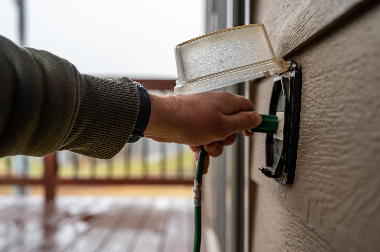 Person plugging in cord to outlet on side of building