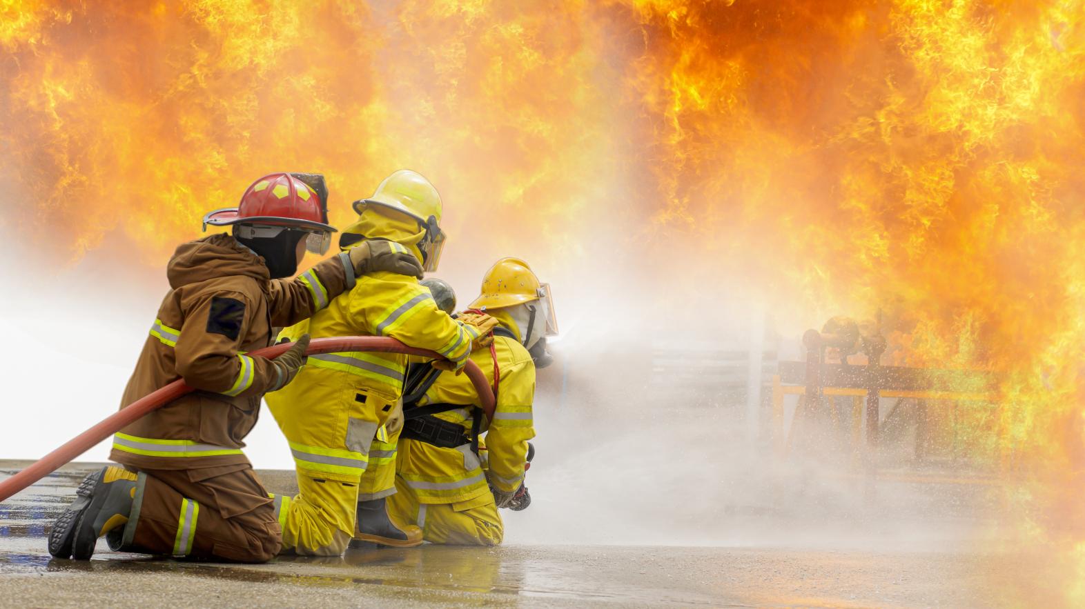 Firefighter training Firefighters using water and fire extinguishers to fight the flames in emergency situations. in a dangerous situation All firefighters wear firefighter uniforms for safety