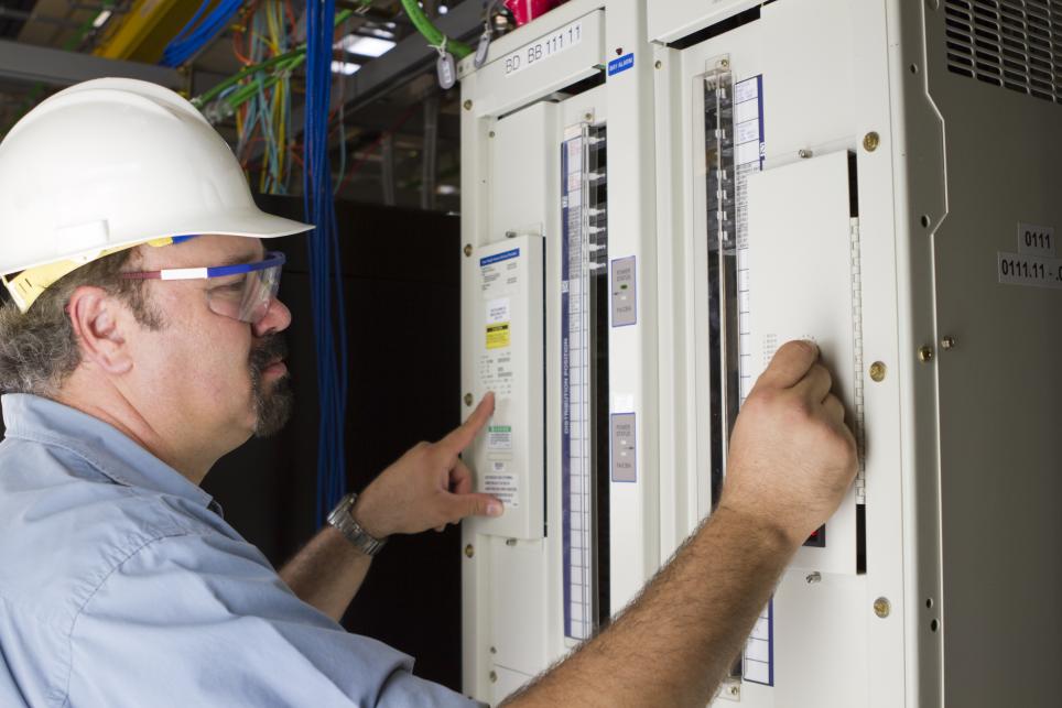 A male electrician inspects and electrical control panel.