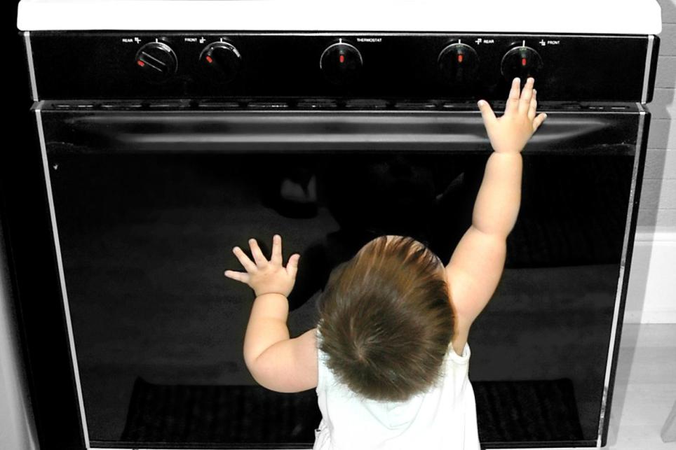 Baby reaching for oven knobs with pan of hot food on range top