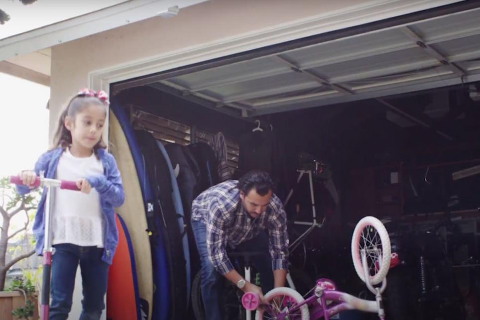 Father working in garage while child plays in driveway