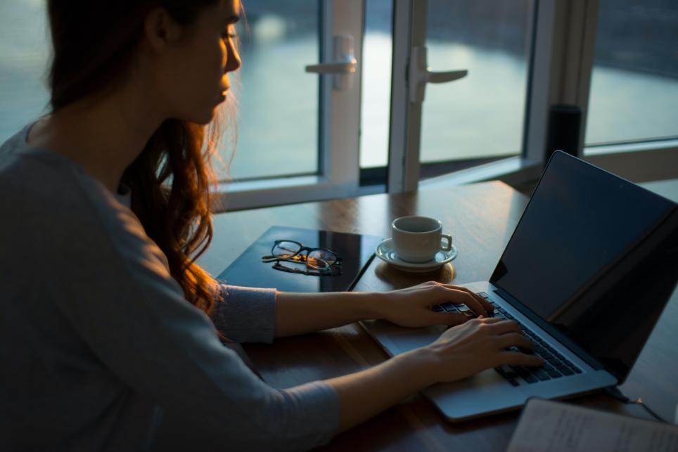 Woman typing at laptop on desk.