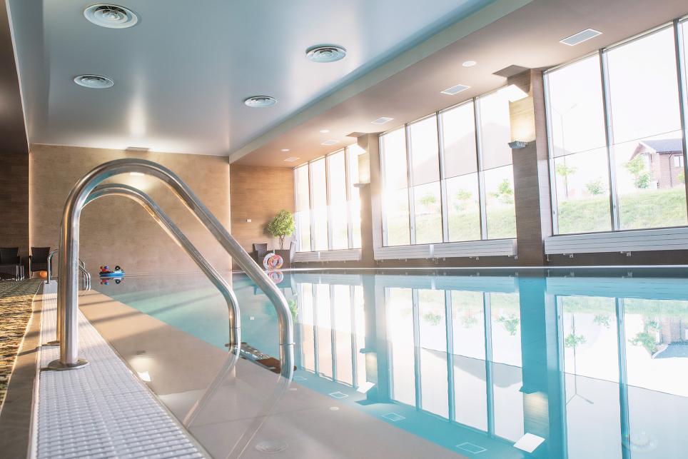 An empty hotel swimming pool area. The water is still and light from the windows shines on the surface of the water.