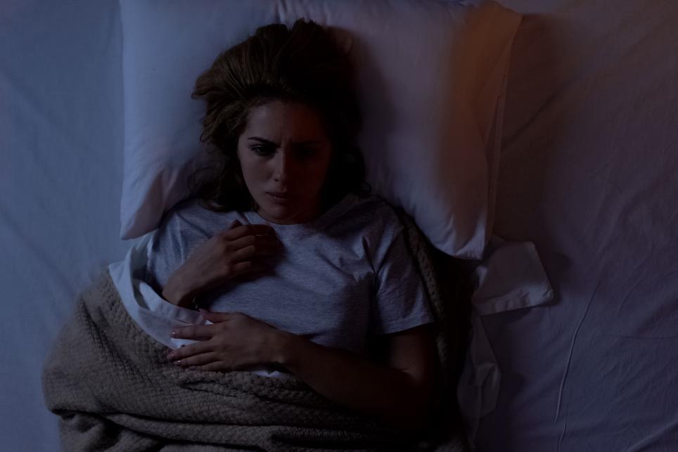 A woman lays in bed with an alarmed facial expression