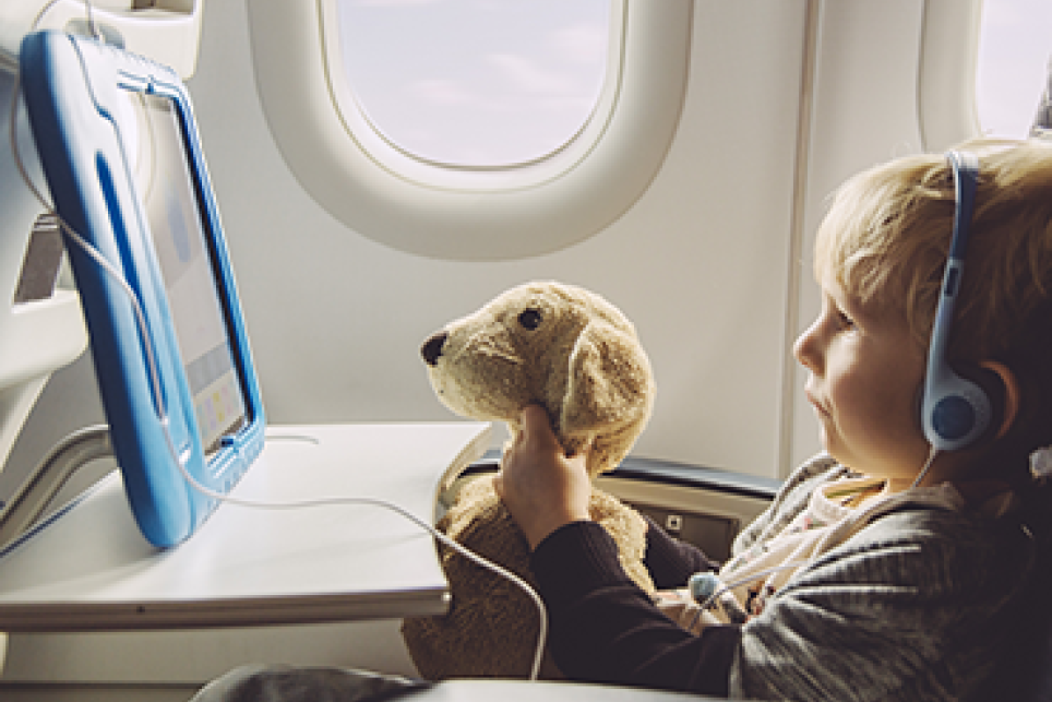 Child with stuffed animal viewing tablet on airplane.