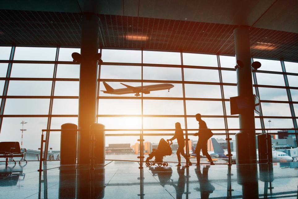 Family Walking through airport - silhouette against tall windows with planes taking off in the background