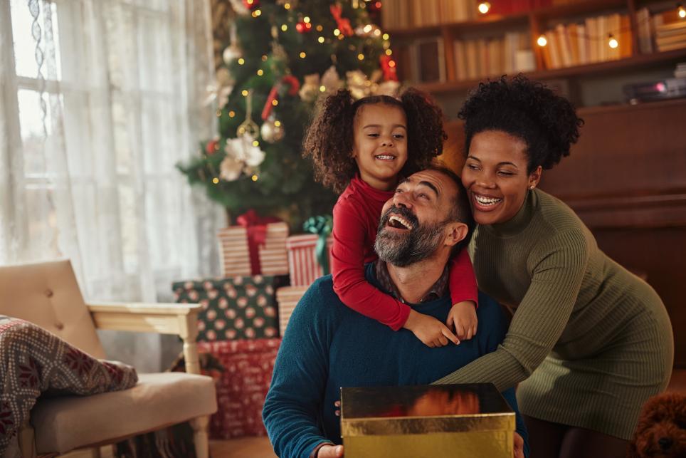 family having happy time together on Christmas. Mom and daughter are hugging dad as he opens his gift