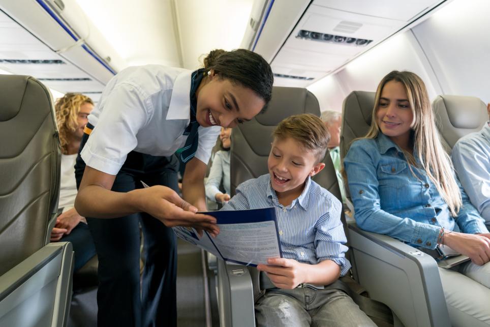 A flight attendant speaks with a boy on board an airplane