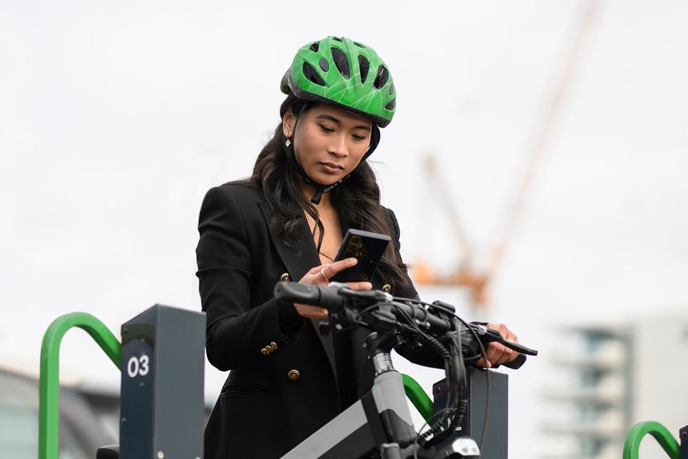 A woman in a helmet checks her phone before getting on her e-bike for a nice ride