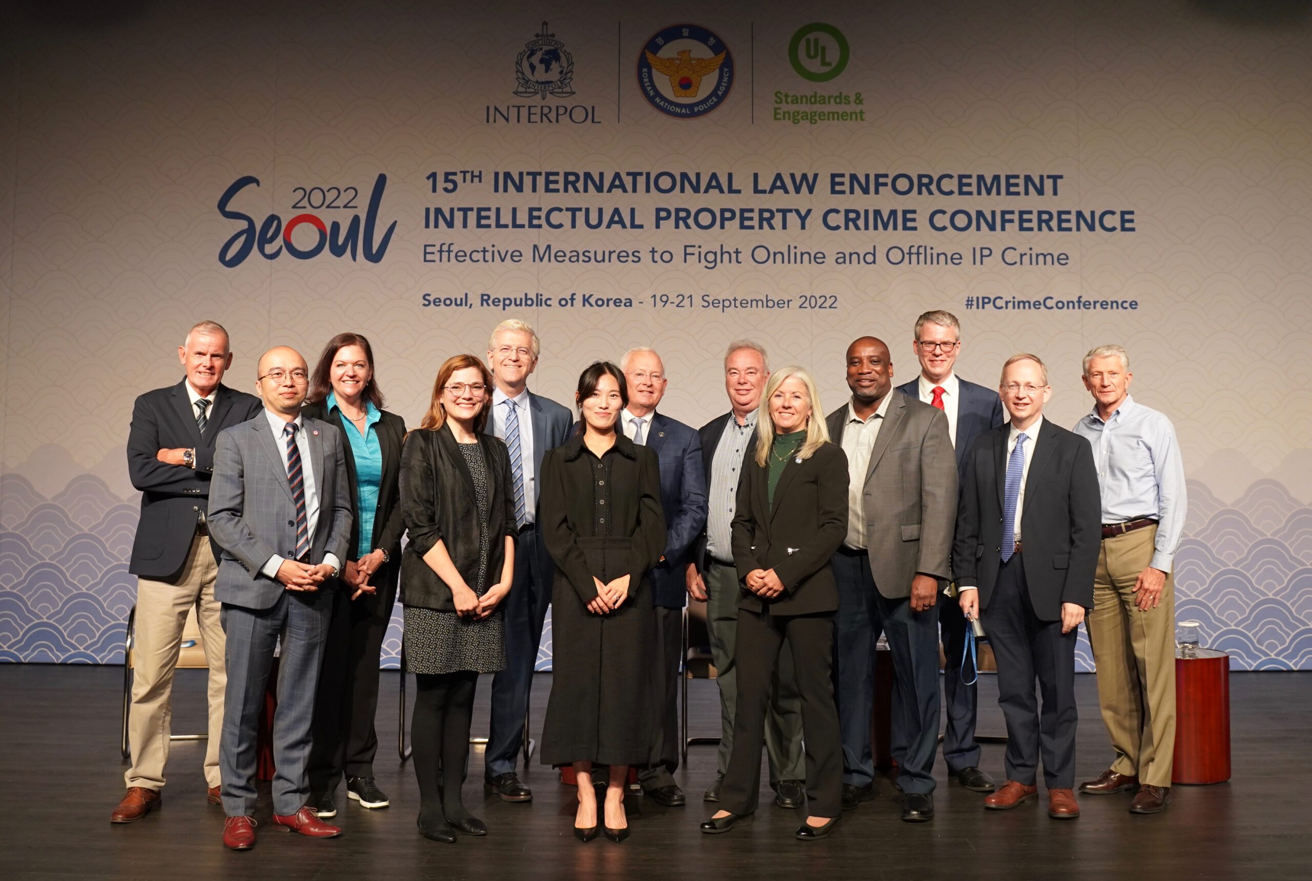 A group of conference attendees, dressed in business attire, stand on stage smiling for a photo at the 15th International Law Enforcement Intellectual Property Crime Conference in Seoul, 2022.