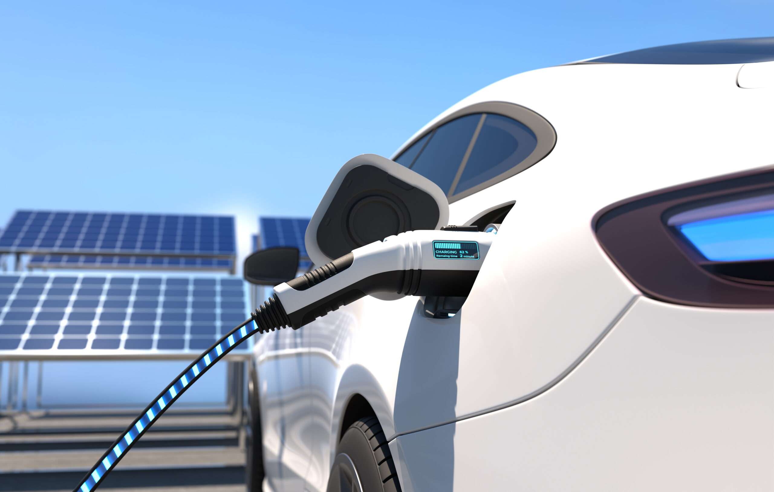 A close-up of an electric car being charged, with a charging cable plugged in. Solar panels are visible in the background under a clear blue sky.