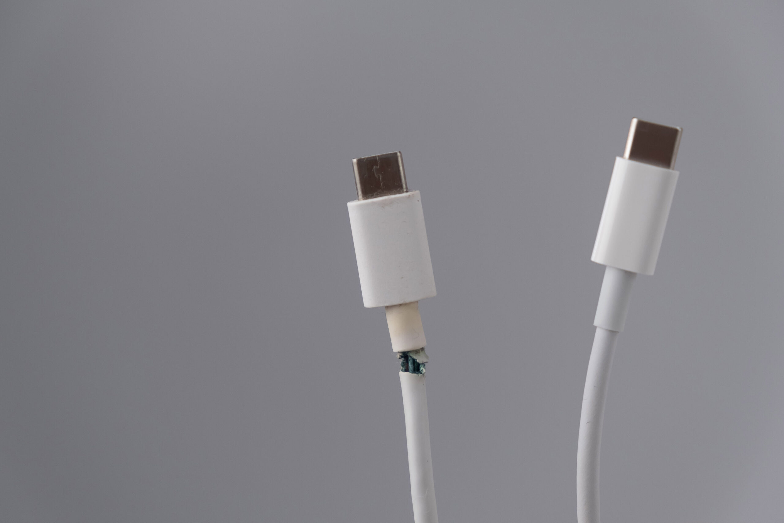 Two white USB-C cables are shown against a plain gray background; one cable has a damaged, frayed area near the connector, while the other is intact.