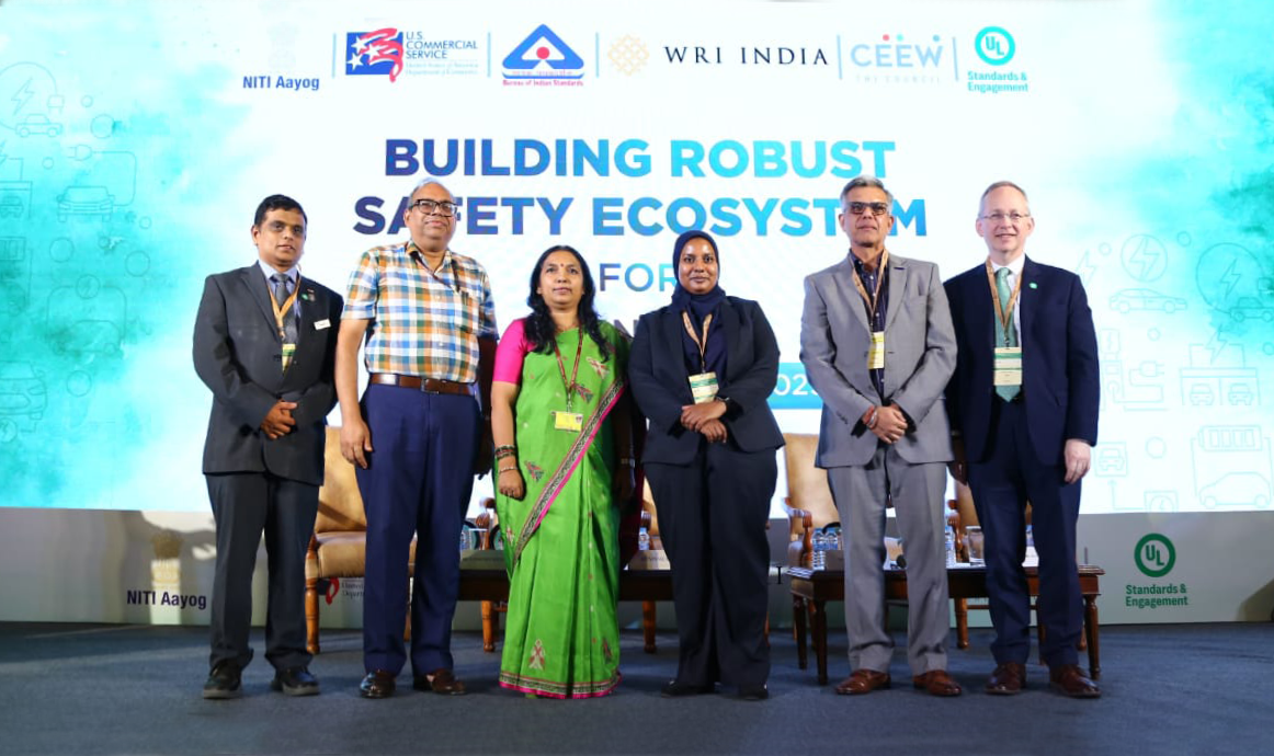 Six people stand on stage at a conference. Behind them is a large sign that reads "Building Robust Safety Ecosystem" with various organization logos and icons related to safety and standards.