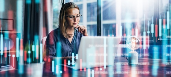 A woman wearing glasses works on a laptop at a desk, with abstract digital financial graphs and data visualizations overlaid, suggesting analysis or trading activity.