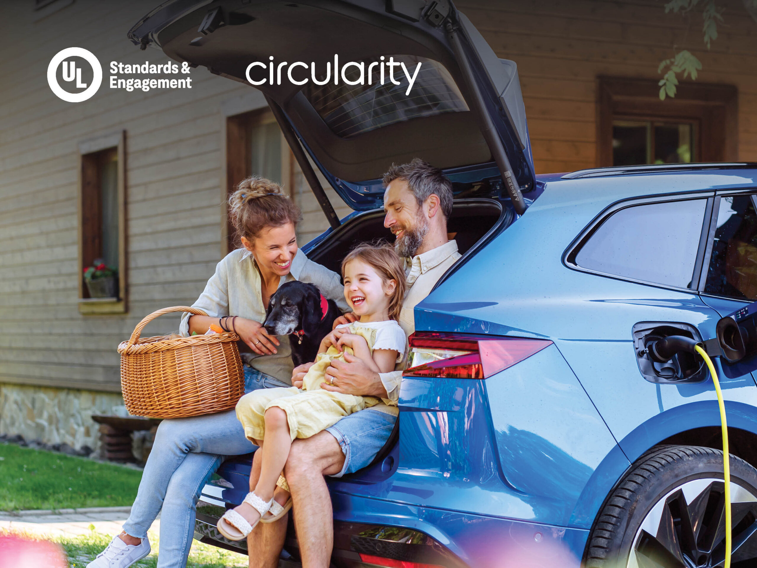 A smiling family with a child and a small dog sit in the open trunk of a blue electric car charging outside a wooden house. The mother holds a picnic basket. Text reads "UL Standards & Engagement" and "circularity.