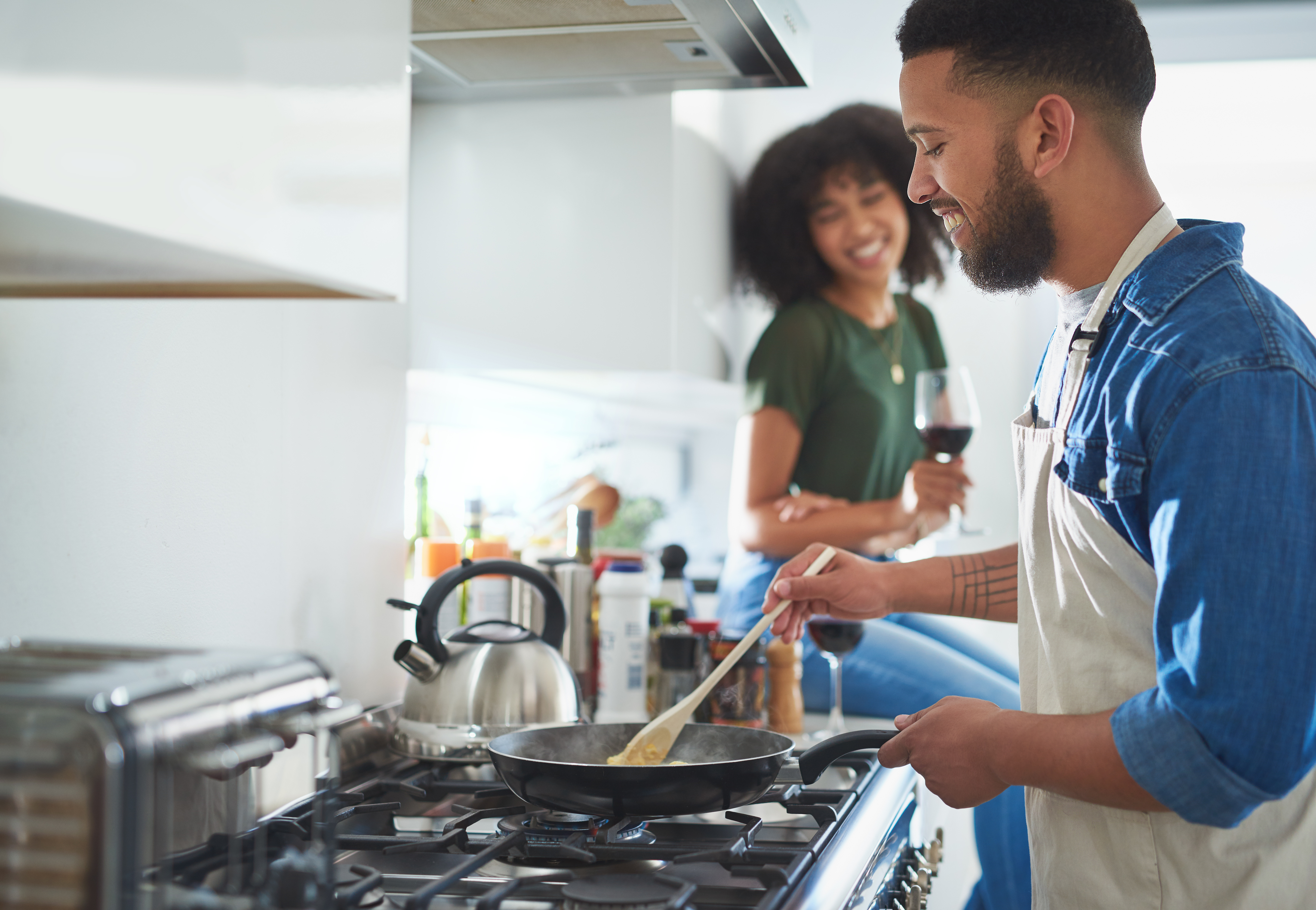 Man cooking on gas range with female seated behind him