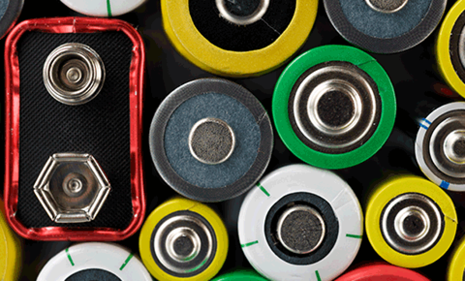 Close-up top view of various batteries, including cylindrical AA, AAA, and a rectangular 9-volt battery, with colorful casings in yellow, green, red, and white, showing the terminals.
