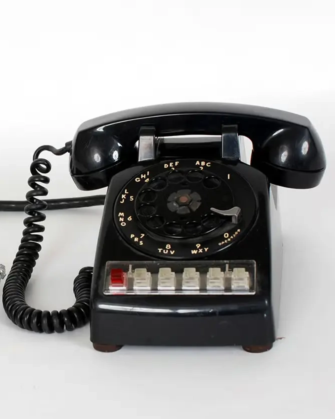 A vintage black rotary dial telephone with push buttons and a coiled cord, set against a plain white background.