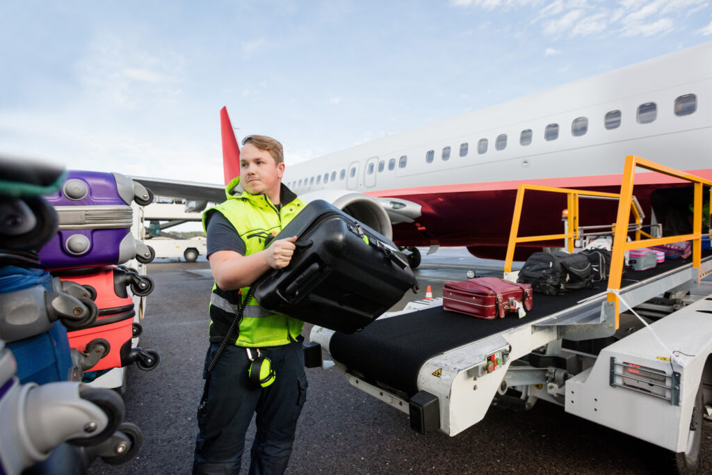 Baggage worker in yellow vest loading checked luggage into the cargo hold of an airplane