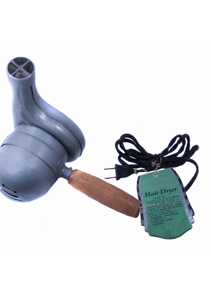 A vintage handheld hair dryer with a metal body, wooden handle, black power cord, and a green instruction tag attached.