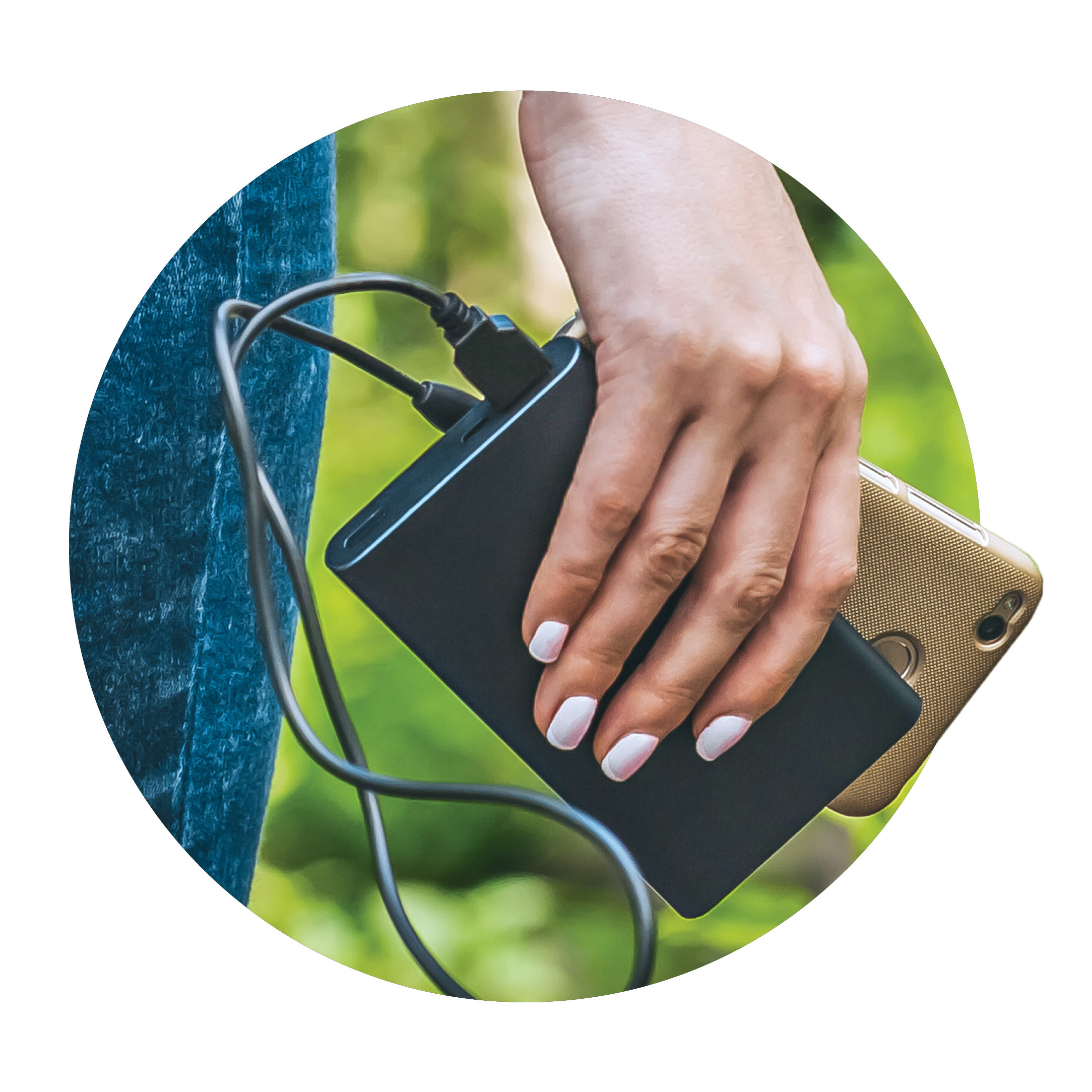 A close-up of a person’s hand holding a smartphone and an external power bank, with a charging cable connecting the two, against a blurred outdoor background.