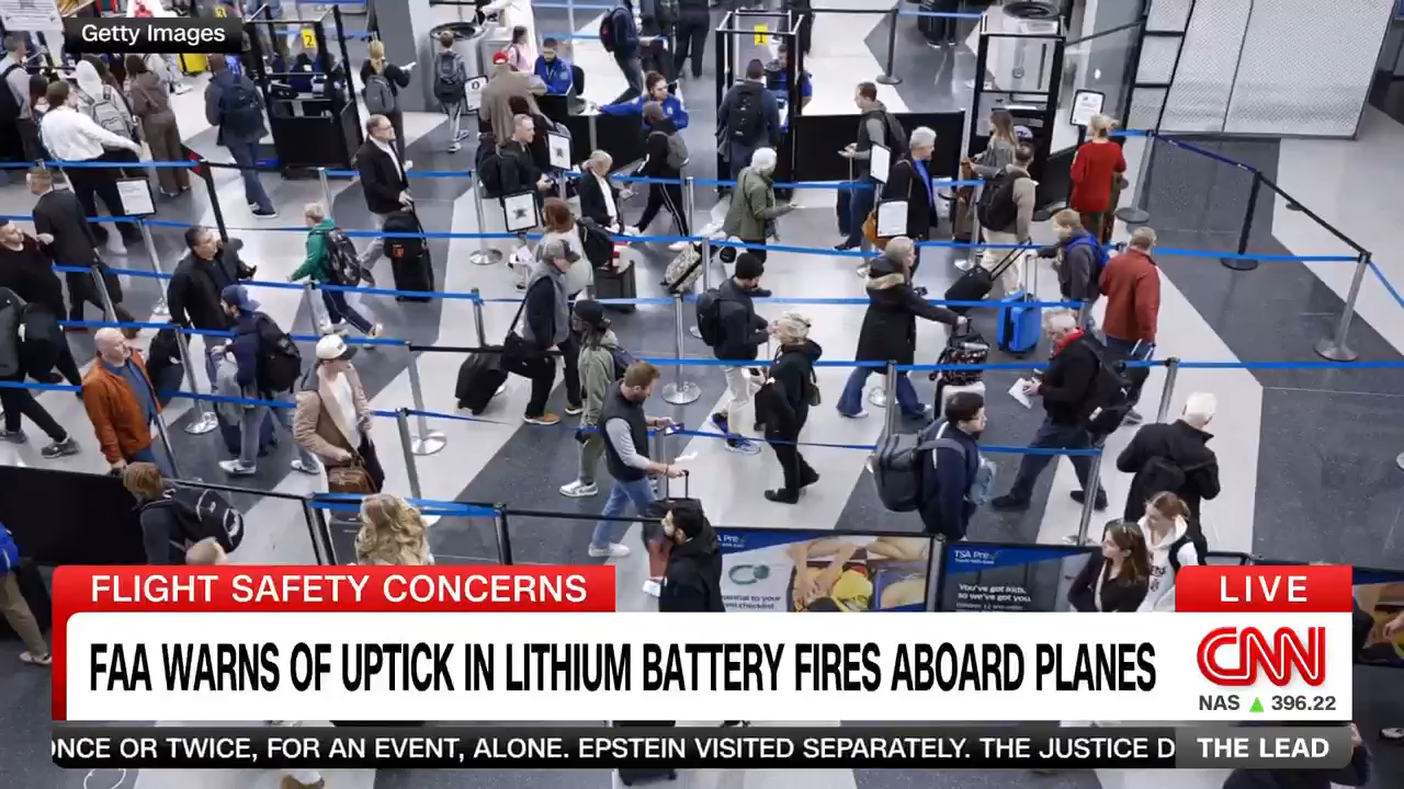 A busy airport security checkpoint with many travelers in line, carrying luggage. A CNN news banner warns of an uptick in lithium battery fires aboard planes, highlighting FAA safety concerns.