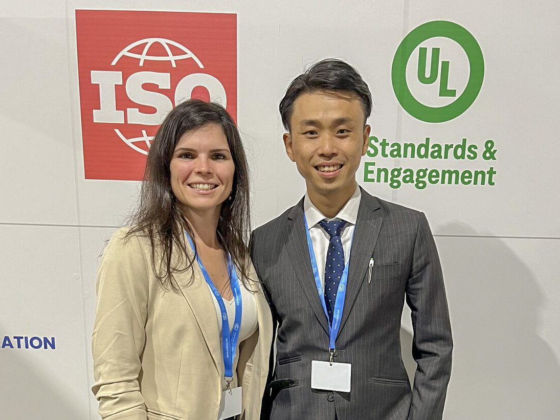 Two people smiling and standing in front of a backdrop with ISO and UL Standards & Engagement logos, both wearing business attire and conference badges.