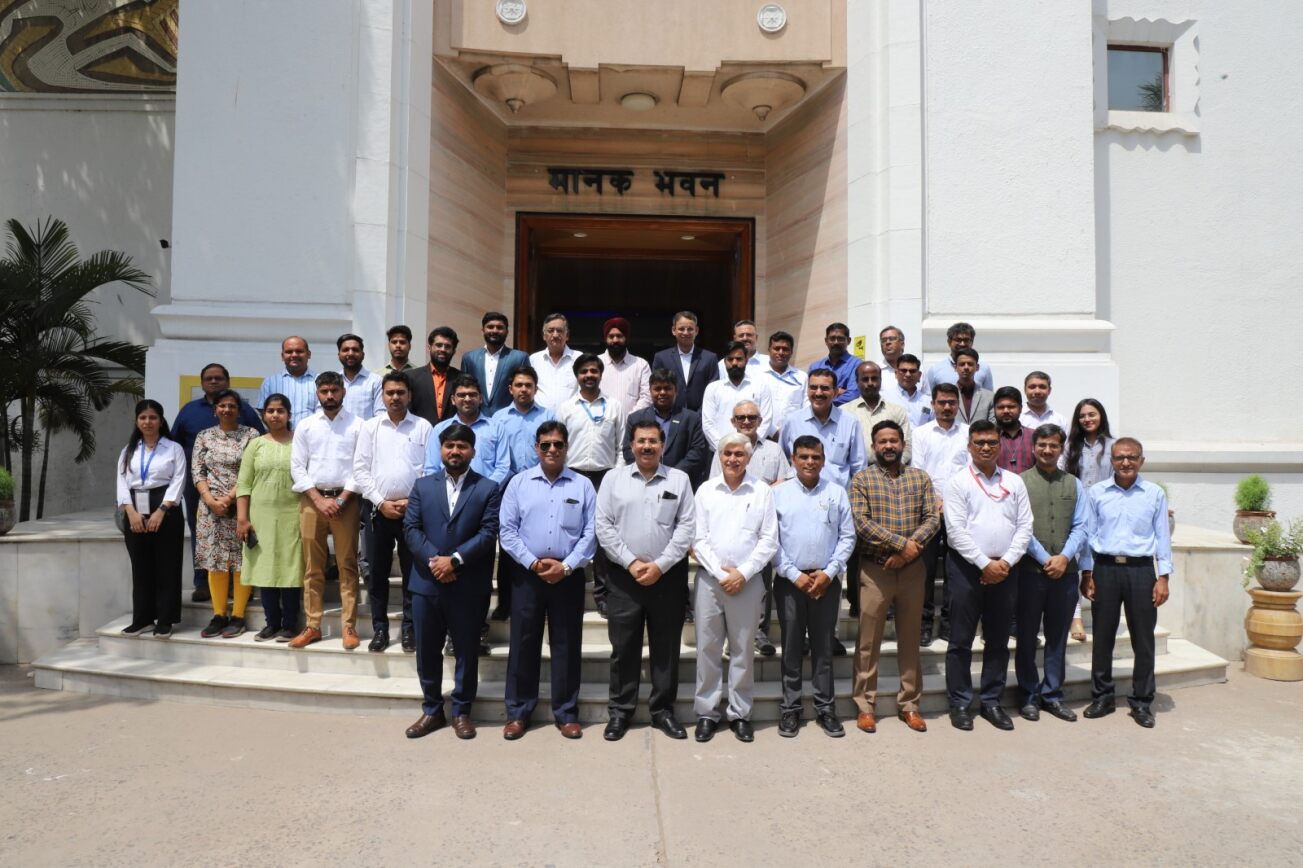 A large group of men and women pose for a photo in front of a building entrance with the sign "राज्य भवन" above the door. The group is dressed in formal and business attire, standing in rows on the steps.