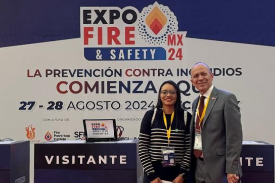 Two people wearing business attire and event badges stand and smile in front of a fire safety expo booth with a sign that reads "Expo Fire & Safety MX24" and event dates, August 27-28, 2024.