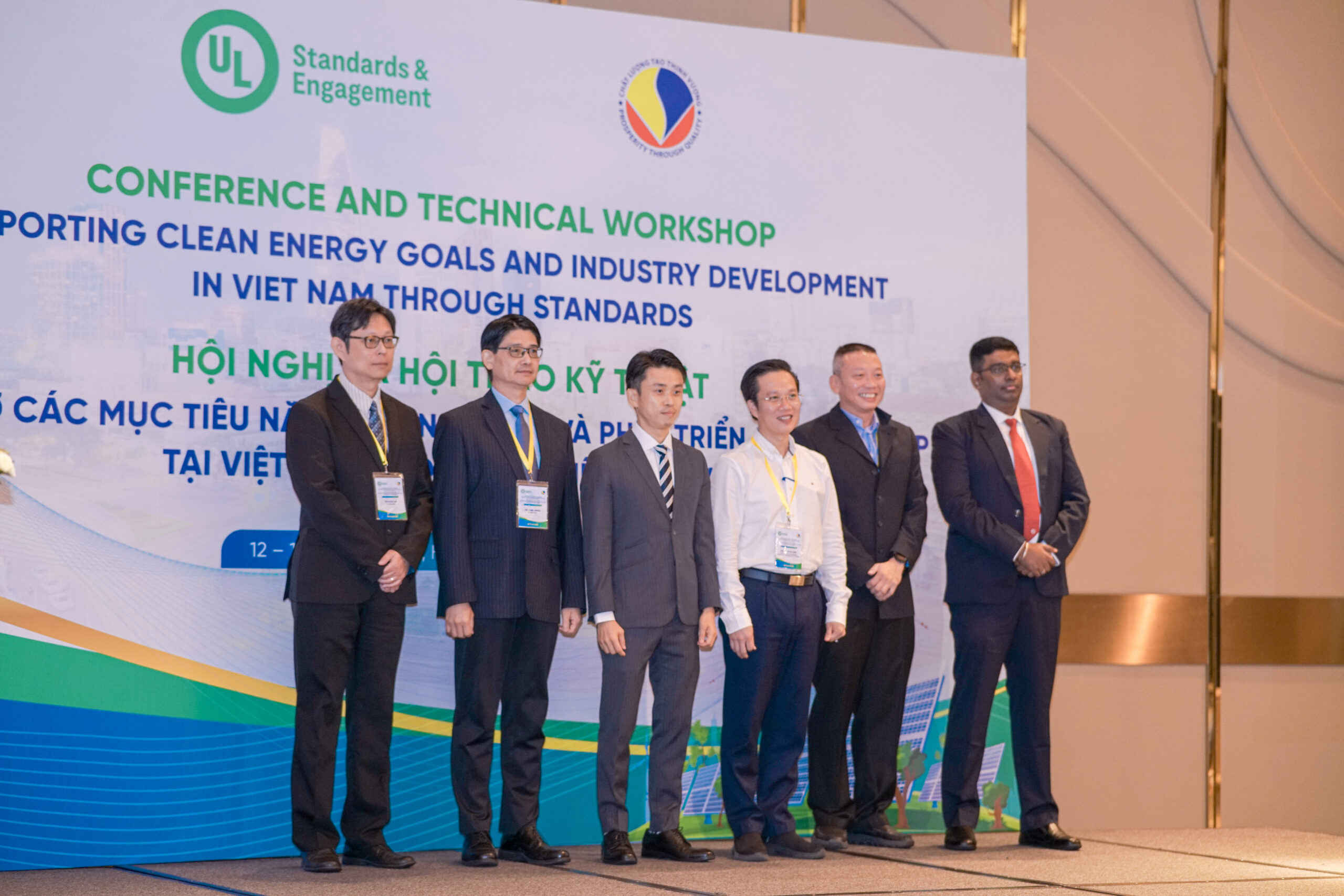 Six men in business attire stand in a row on stage at a conference and technical workshop on clean energy and industry development in Vietnam, with a large event banner in the background.