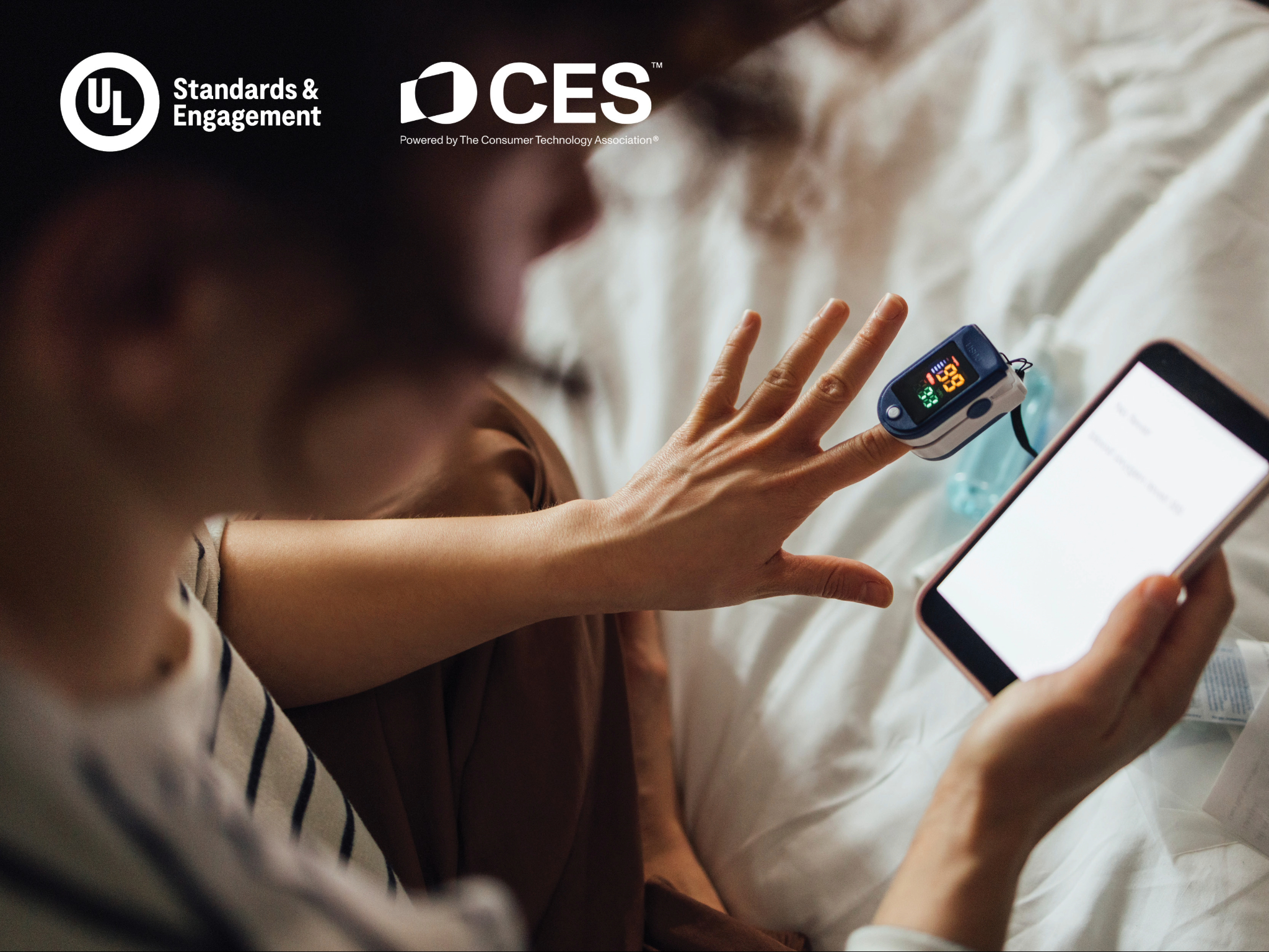 A person checks their blood oxygen level with a fingertip pulse oximeter while holding a smartphone. Logos for UL Standards & Engagement and CES are visible in the upper left corner.