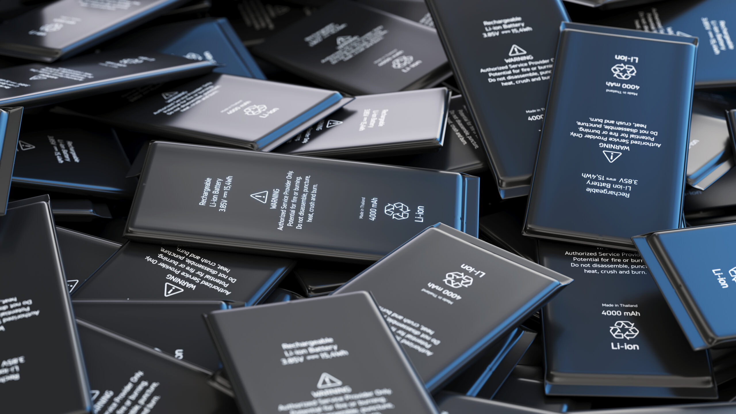A large pile of rectangular lithium-ion smartphone batteries, each labeled with technical specifications, warnings, and recycling symbols, arranged in a scattered manner.