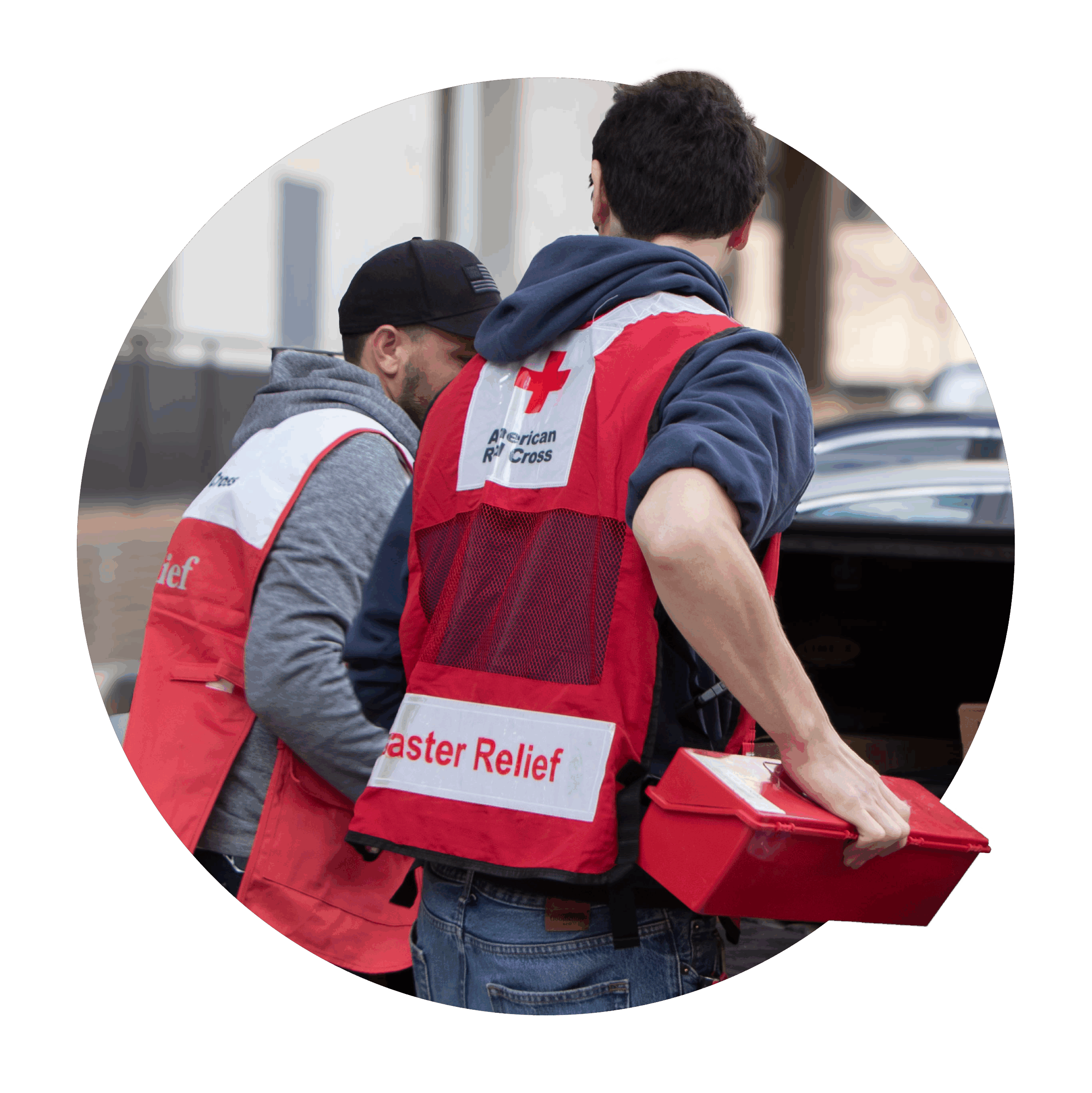 Two people wearing American Red Cross "Disaster Relief" vests, in partnership with UL Standards & Engagement (ULSE), unload supplies from a car. One person is holding a red box, and both are focused on their relief work.
