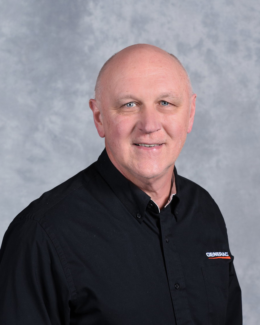 A man wearing a black button-up shirt with a small embroidered "GENERAC" logo, poses and smiles in front of a gray mottled background.
