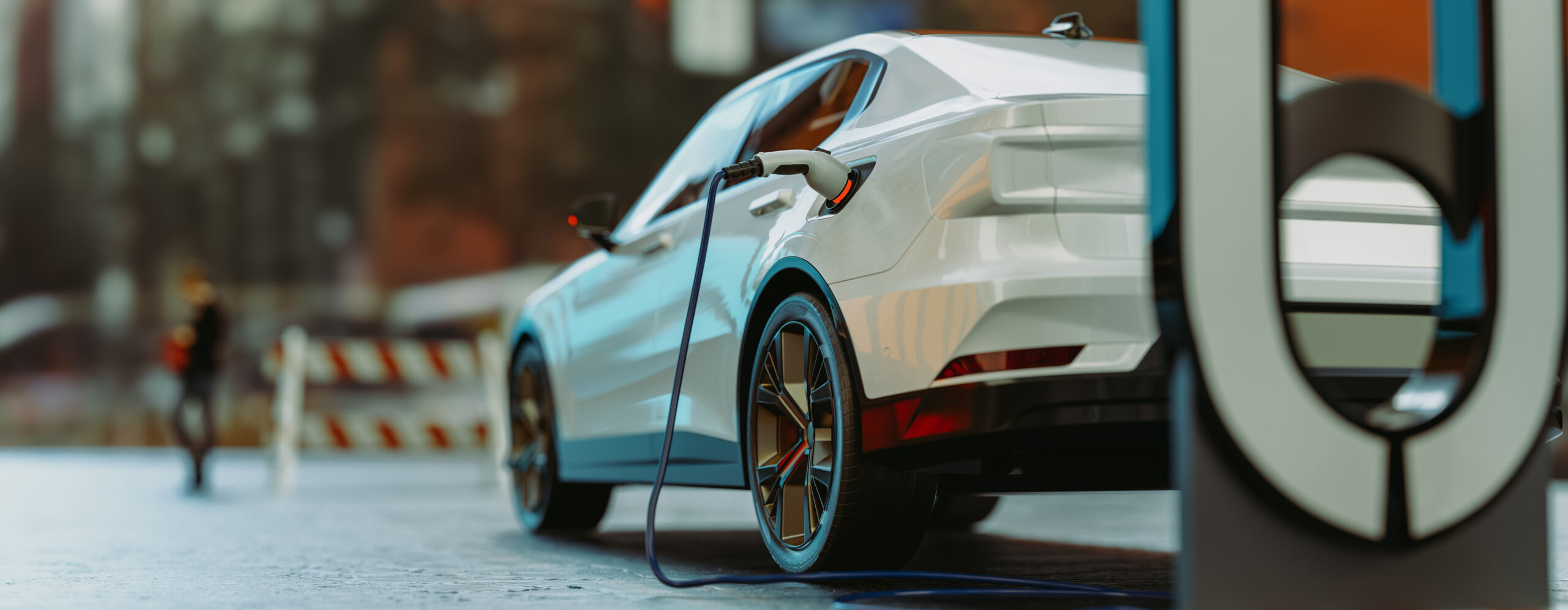 A white electric car is parked and charging at a public charging station on a city street. The charging cable is connected to the car, and blurred urban elements are visible in the background.