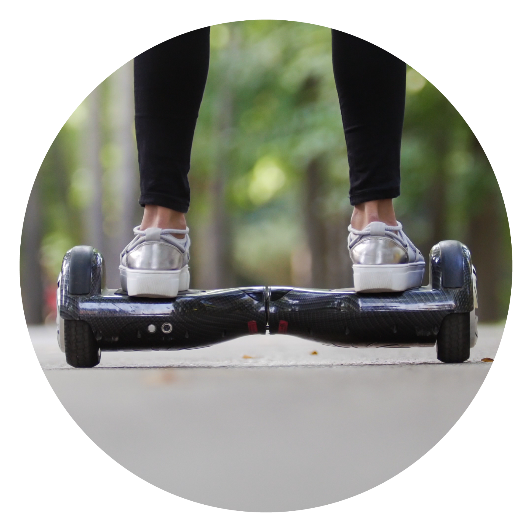 Close-up of a person wearing silver sneakers and black pants riding a black hoverboard on an outdoor path with blurred green trees in the background.