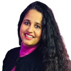A woman with long, wavy dark hair smiles at the camera. She is wearing a pink turtleneck under a black jacket. The background is plain white.