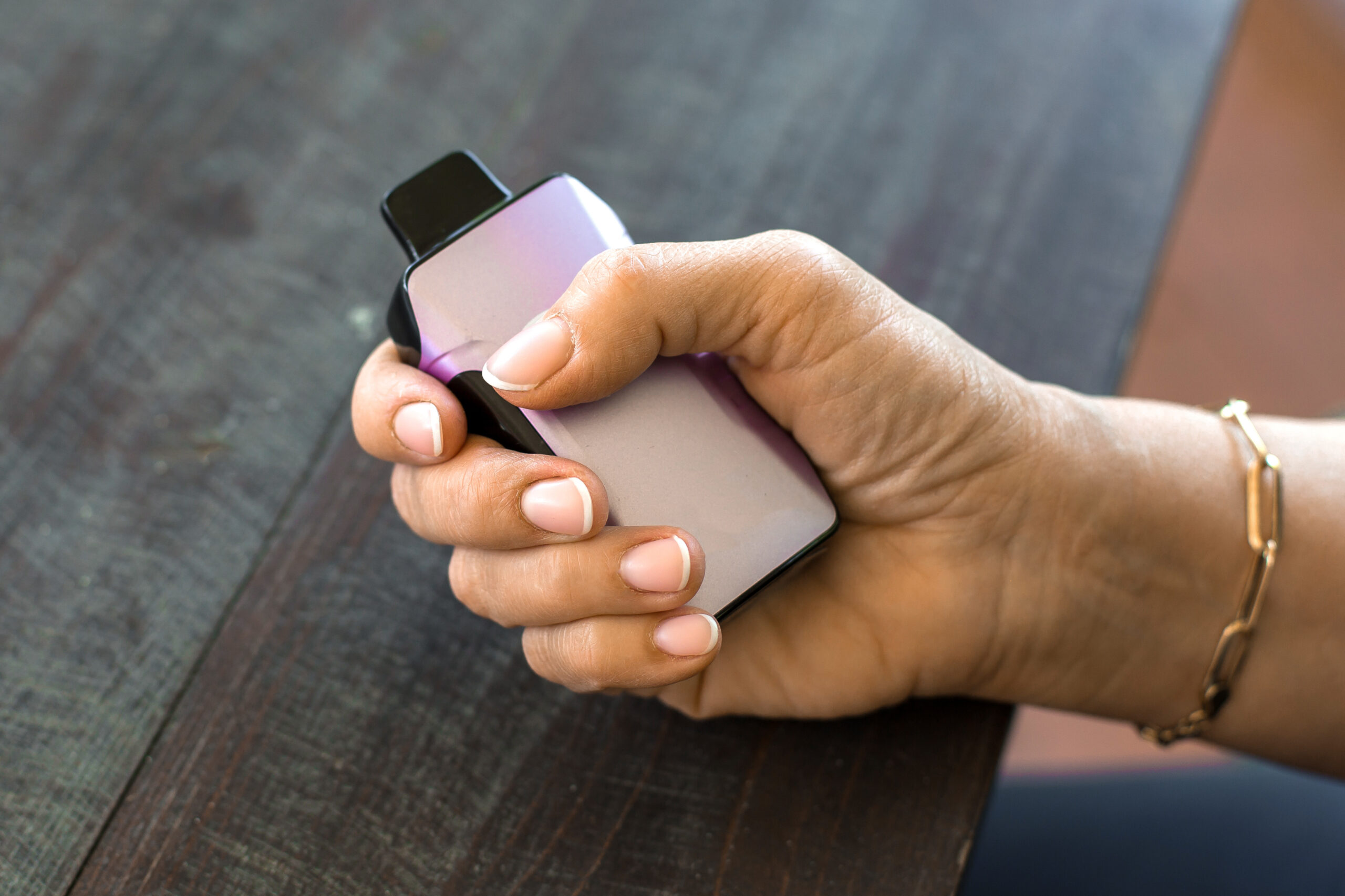 A hand holding a rectangular, iridescent purple disposable vape device.