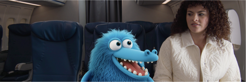 A woman with curly hair sits on an airplane next to a blue, furry animated creature with a big smile and wide eyes, both unaware of the aviation risks like a lithium-ion battery fire on plane journeys.